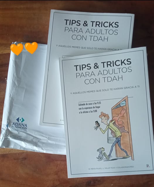 Dos libros titulados 'TIPS & TRICKS PARA ADULTOS CON TDAH' sobre el trastorno del déficit de atención e hiperactividad en adultos, sobre una mesa con un paquete de envío de la FUNDACION ADANA.